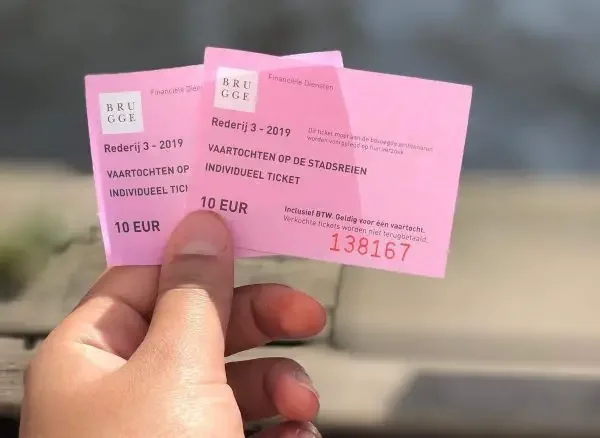 A hand holding two pink tickets