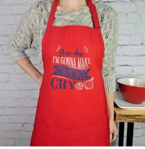 A woman wearing a red apron with "one day, I will make onions cry"