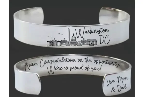 A silver cuff bracelet with the skyline of Washington DC and a personalized message
