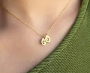 A golden necklace with two halves of an avocado