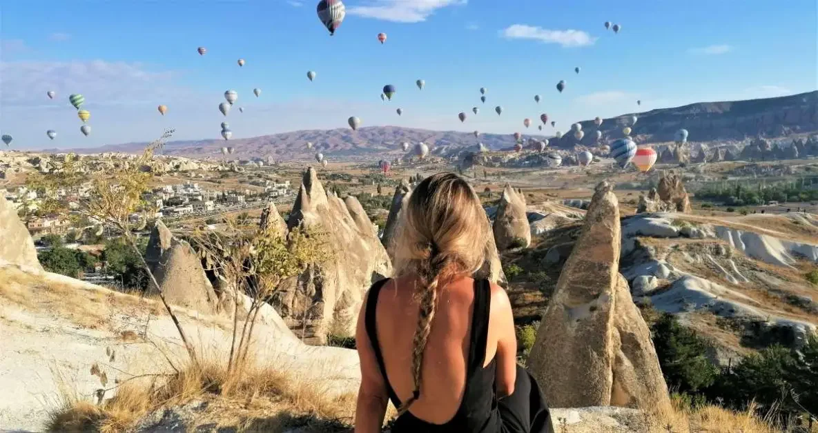 Photo of a woman's back looking at a landscape with hot air balloons