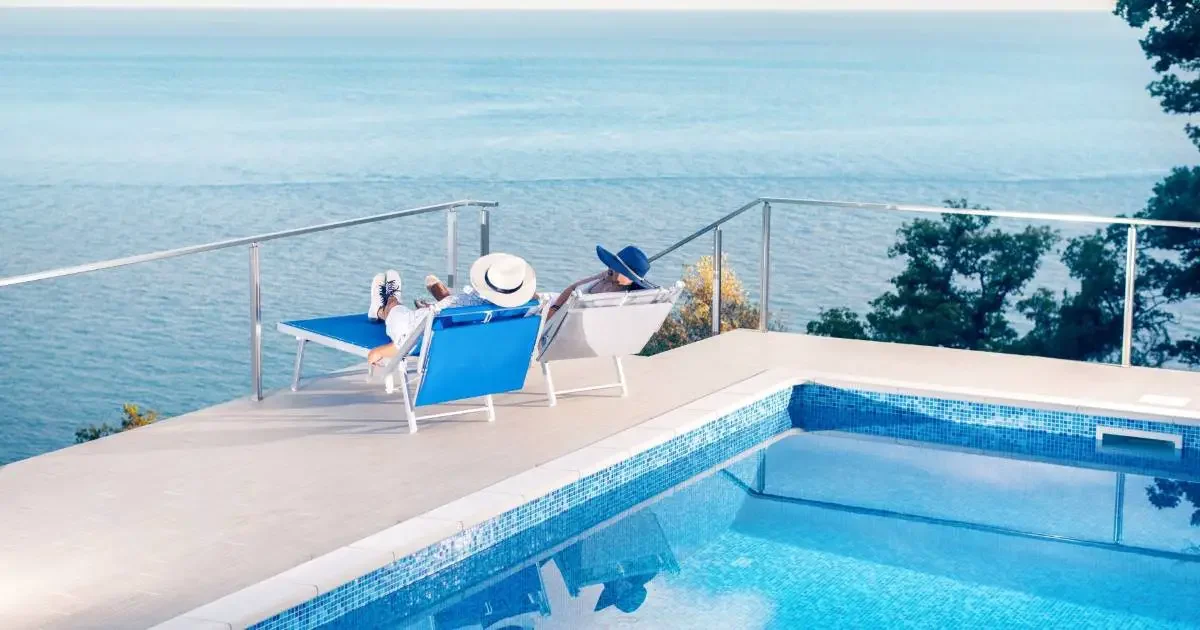 Two people enjoying a luxury vacation at the an infinity pool looking over the sea