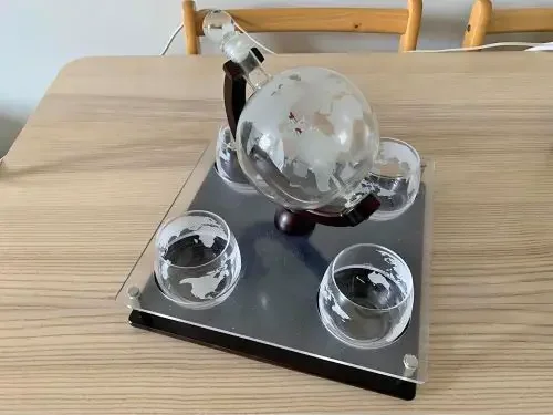 A glass decanter that is shaped like the globe and comes with four whisky glasses