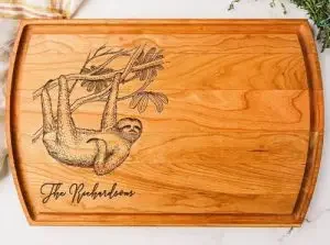 A bamboo cutting board with a family name etched and a sloth etched