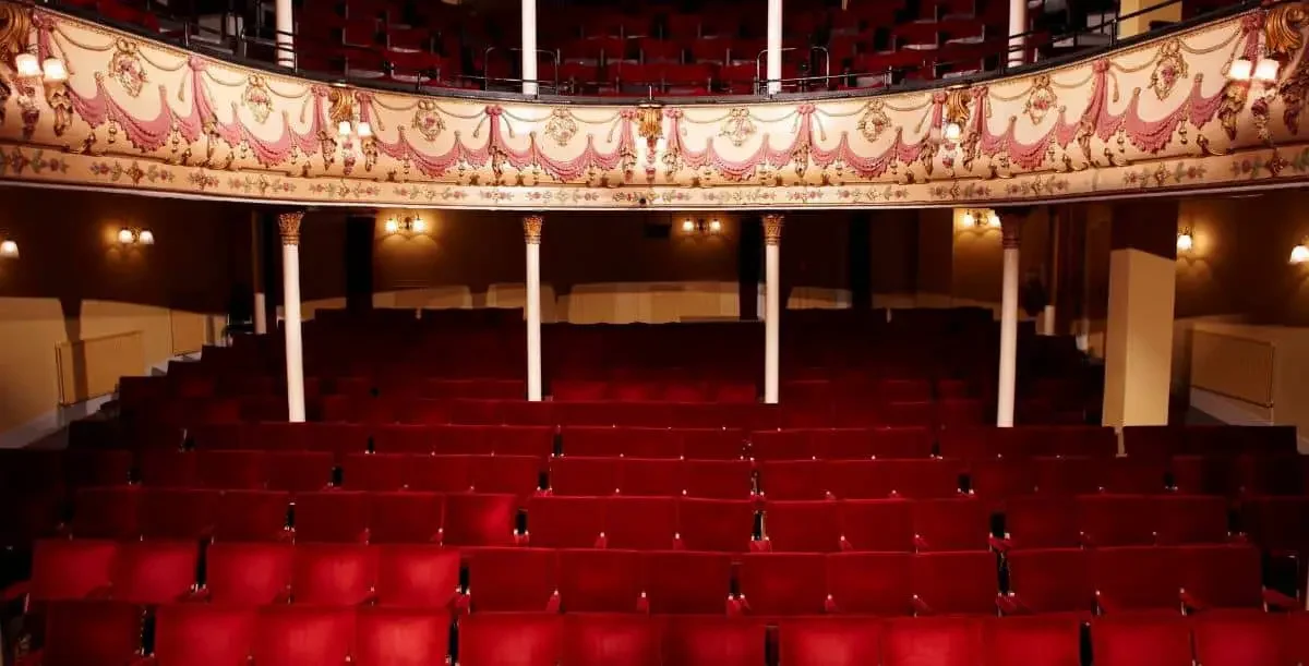 A photo of a theatre with red chairs and a second level