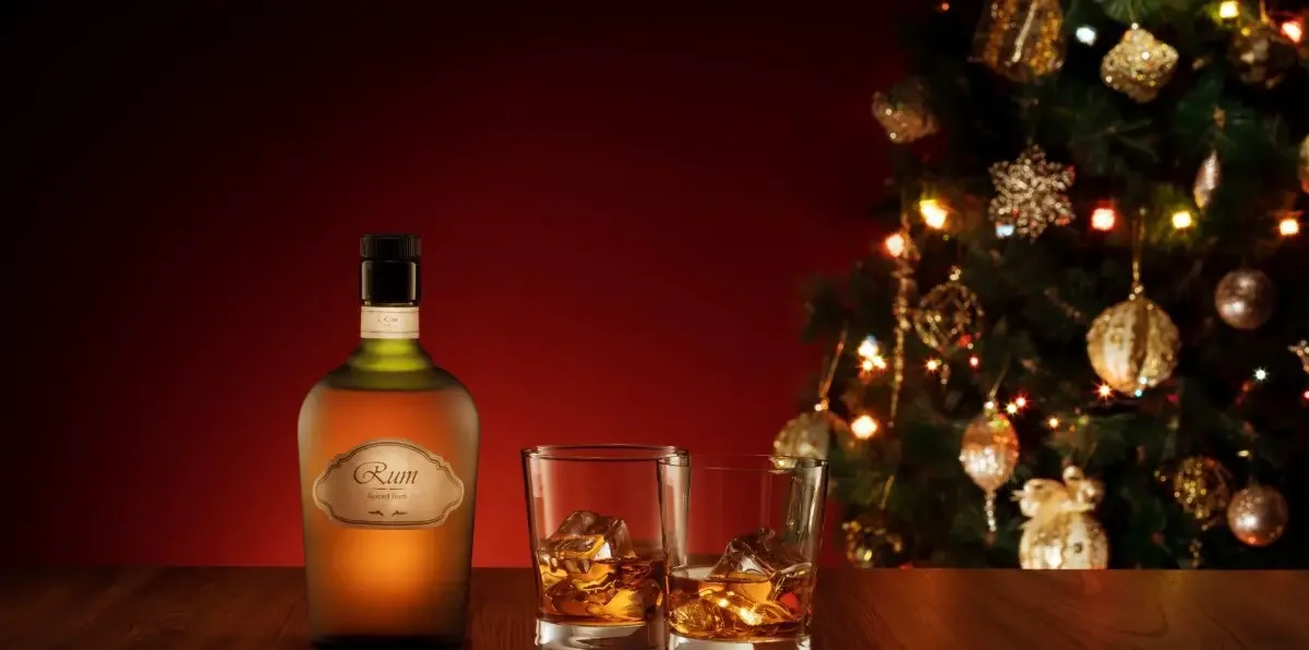 A photo of a bottle of rum with two glasses and a Christmas tree in the background